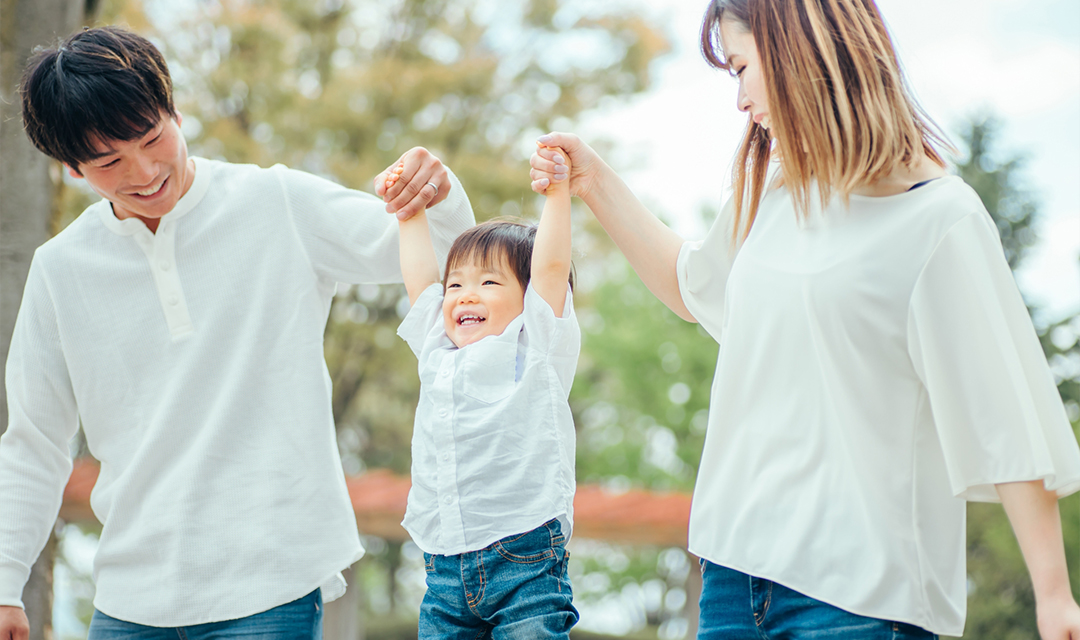 手をつなぐ父親と子どもと母親の写真